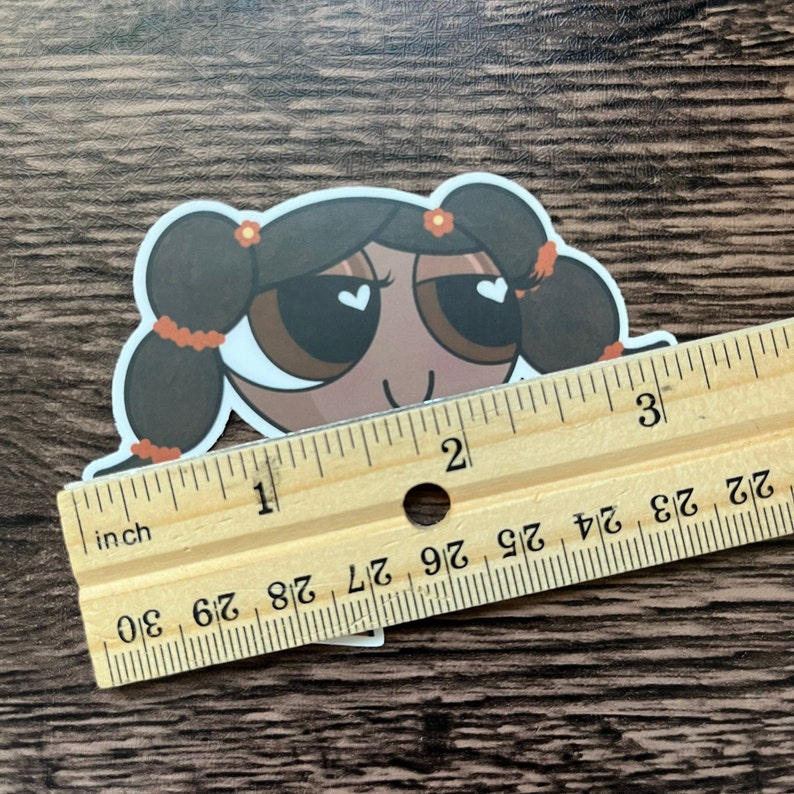 May include: A sticker of a cartoon character with brown hair, brown eyes, and a light brown complexion. The character has a white heart in each eye and is wearing a red flower in their hair. The sticker is about 1 inch tall.