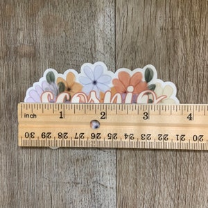 May include: A sticker with the word "Cosmic" written in a white script font with a floral design around it. The flowers are in shades of purple, orange, and yellow.