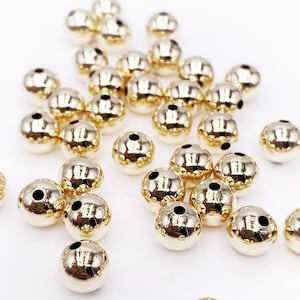 May include: A pile of gold-colored metal beads with a textured surface. The beads have a small hole in the center for stringing.