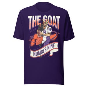 May include: Purple t-shirt with a graphic of a goat-like figure in a football uniform holding a football. The text "THE GOAT" and "NUMBER NINE" are displayed on the shirt. The shirt also has the text "EST. 2018".