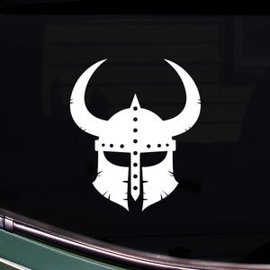 Puede incluir: Calcomanía blanca de casco vikingo con cuernos curvos, remaches y protector facial. El diseño de silueta es adecuado para aplicar en la ventana de un coche u otra superficie lisa. Representación gráfica audaz de un casco vikingo.