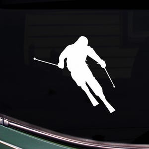 Peut inclure: Autocollant en vinyle blanc représentant un skieur en mouvement, avec des skis et des bâtons. Le skieur est représenté dans une pose dynamique, glissant sur une pente. L'autocollant est conçu pour être appliqué sur une vitre de voiture ou une surface similaire.