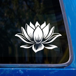 Peut inclure: Autocollant de fleur de lotus blanche. L'autocollant présente un contour détaillé d'une fleur de lotus, symbole de pureté et d'illumination. L'autocollant est affiché sur une fenêtre, avec un cadre de véhicule bleu visible.