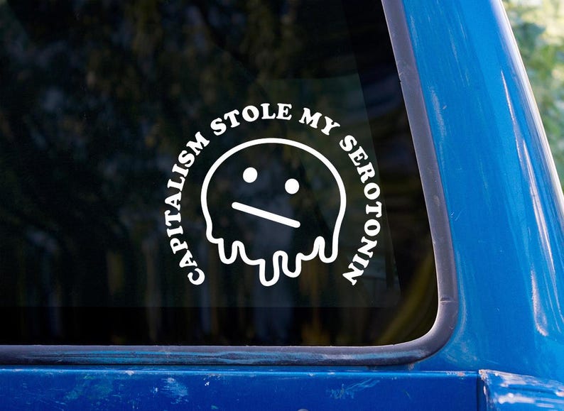 May include: White vinyl sticker with the text "CAPITALISM STOLE MY SEROTONIN" in a circular design around a sad-faced, melting blob graphic. The sticker is affixed to a blue vehicle window.