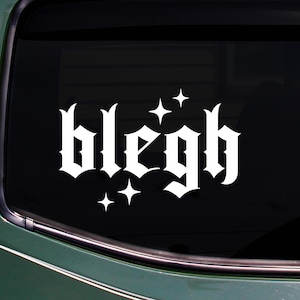 以下が含まれることがあります： ゴシック体で「blegh」という言葉が書かれた白いビニールステッカー。4つの星が添えられています。ステッカーは車の窓に貼られており、緑色の車体が見えます。
