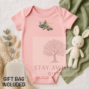 May include: A light pink baby onesie with a helicopter graphic. The onesie has short sleeves and snap closures. A white gift bag and a crocheted bunny are also in the image. The text "GIFT BAG INCLUDED" is visible.