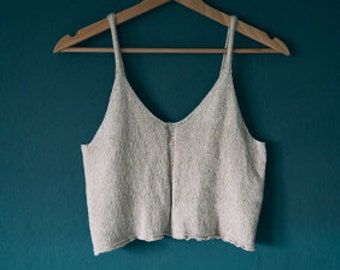 May include: A cream-colored knitted tank top with a V-neck and a scalloped hem.