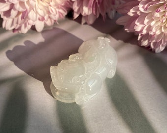 May include: A white jade carving of a mythical creature, possibly a dragon or a lion, with intricate details. The carving is smooth and polished, and the jade has a translucent quality.