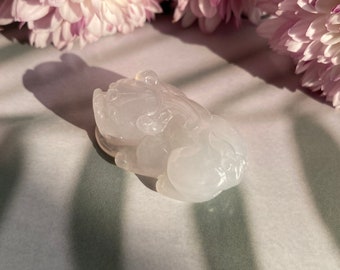 May include: A white jade carving of a mythical creature, possibly a dragon or a lion, with intricate details. The carving is smooth and polished, and the jade has a translucent quality.