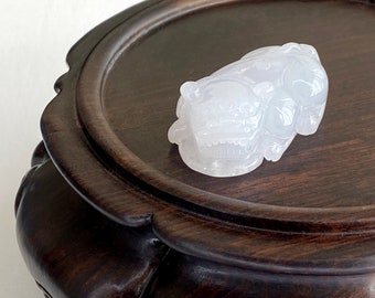 May include: A white jade carving of a mythical creature, possibly a dragon or lion, resting on a dark wood pedestal.