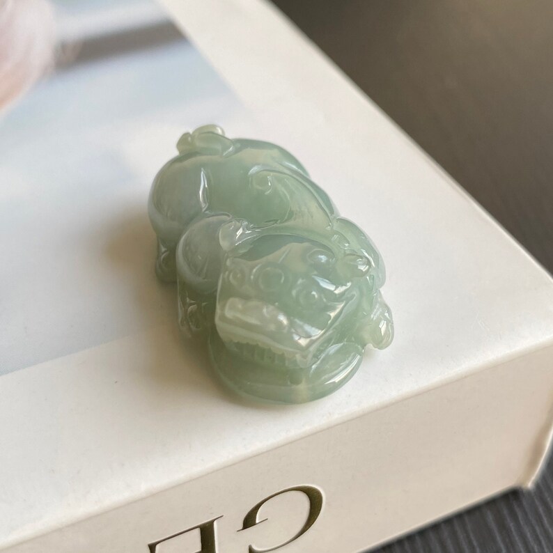 May include: A jade green pendant carved in the shape of a mythical creature. The pendant is smooth and polished, with intricate details.