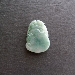 以下が含まれることがあります： 複雑なデザインが彫刻された緑色の翡翠のペンダント。ペンダントはひょうたんの形をしており、滑らかで磨かれた表面をしています。