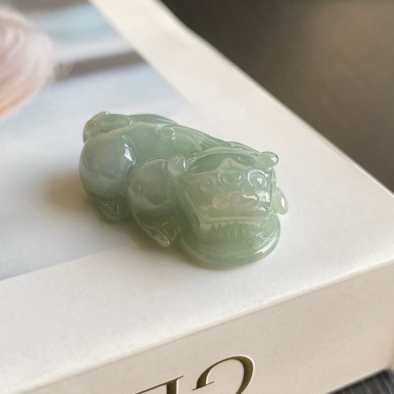May include: A jade green jadeite pendant carved in the shape of a mythical lion, a traditional Chinese symbol of protection and good luck.