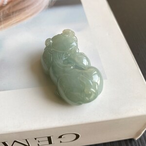 May include: A jade pendant carved in the shape of a mythical creature. The pendant is a light green color and has intricate details.
