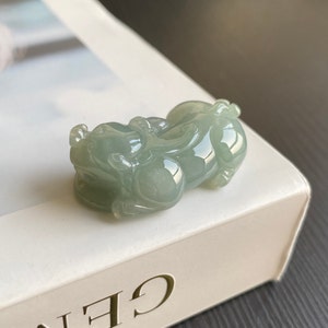 May include: A jade green jadeite carving of a mythical creature, possibly a dragon or a lion, with intricate details. The carving is smooth and polished, with a light green hue.