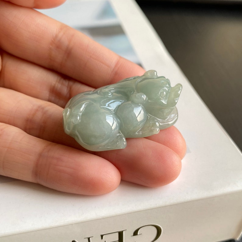 May include: A jade green carved pig pendant. The pig is lying down with its head turned to the side. The pendant is smooth and polished.