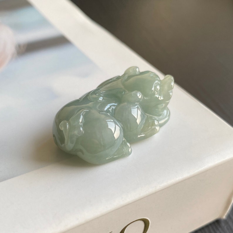 May include: A jade green jadeite carving of a mythical creature, possibly a dragon or a lion, with a crouching pose. The carving is detailed and intricate, with a smooth, polished finish.