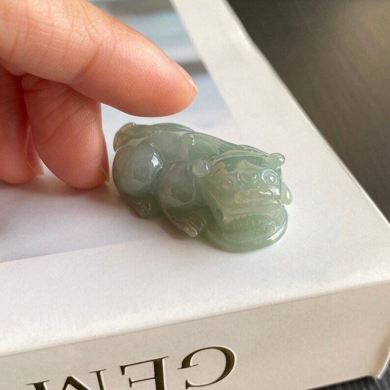 May include: A small, jade green, carved figurine of a mythical lion. The figurine is lying on its belly with its head raised and its mouth open.