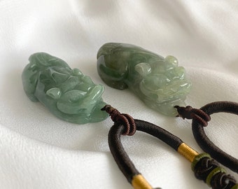 May include: Two jade green pendants carved in the shape of mythical creatures, each with a brown cord attached.