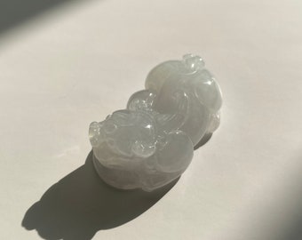 May include: A white jade pendant carved in the shape of a mythical creature. The pendant is smooth and polished, with intricate details.