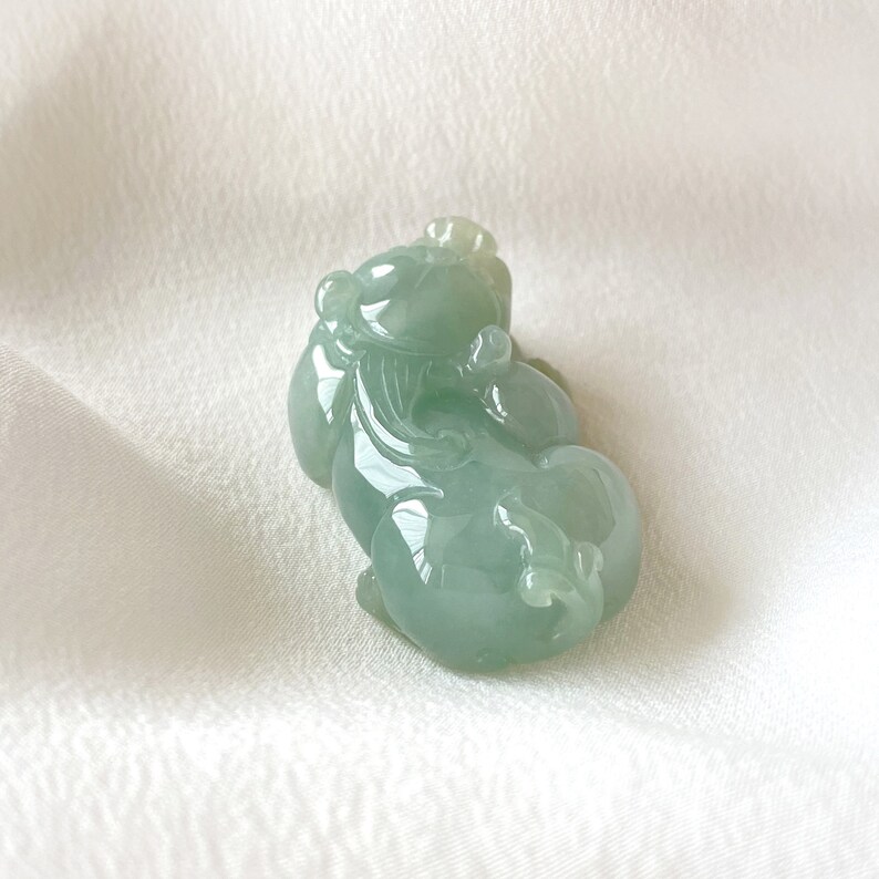 May include: A jade green carved pendant in the shape of a mythical creature. The pendant is smooth and polished, with intricate details.