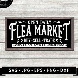 May include: A rectangular sign with a wooden frame, featuring the words "FLEA MARKET" in large white letters on a black background. The sign also includes the phrases "OPEN DAILY" and "BUY SELL TRADE". The sign is on a white wooden background.
