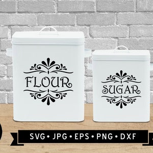 May include: Two white metal canisters with black lettering and decorative flourishes. The larger canister says "Flour" and the smaller canister says "Sugar".