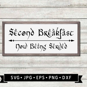 May include: A white sign with black text that reads "Second Breakfast Now Being Served" in a stylized font. The sign is framed in a brown frame and is displayed against a woodgrain background.