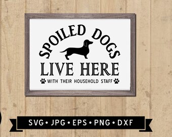 Könnte beinhalten: Ein schwarz-weißes Schild mit dem Text "Spoiled Dogs Live Here With Their Household Staff" und einer Silhouette eines Dackels. Das Schild ist in einem braunen Holzrahmen gerahmt.