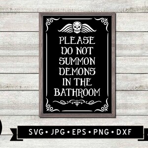 May include: A black and white sign with a skull and wings graphic and the text "PLEASE DO NOT SUMMON DEMONS IN THE BATHROOM". The sign is framed in a dark wood frame.