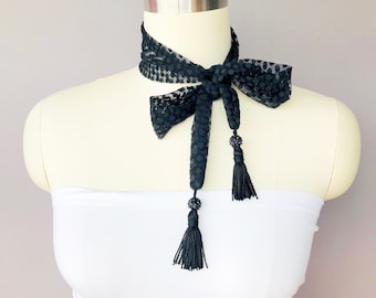 May include: Black lace choker with polka dots and two black tassels. The choker is tied in a bow at the front.