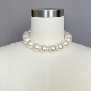 May include: A white pearl necklace with large, round pearls. The necklace is on a white mannequin.