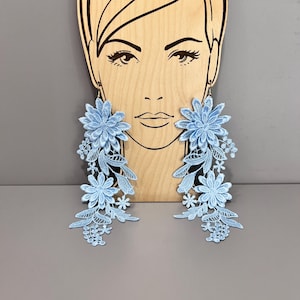 May include: A pair of long, light blue floral earrings. The earrings are made of delicate lace and feature a cluster of flowers at the top.