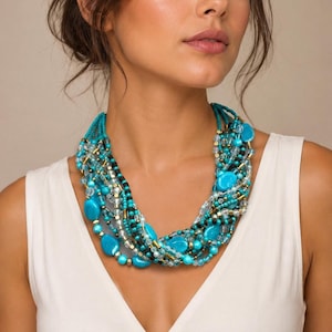 May include: A multi-strand statement necklace featuring a vibrant mix of turquoise blue, clear, and black beads. The design incorporates smooth oval-shaped turquoise stones, small metallic gold spacers, and faceted clear crystals arranged in a layered style.