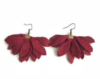 Puede incluir: Un par de pendientes de cuero burdeos con diseño de flor. Los pendientes están hechos de varias capas de pétalos de cuero y tienen un simple gancho dorado.