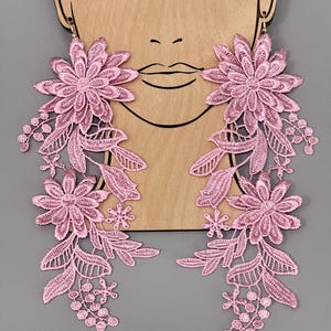 May include: A pair of pink floral lace dangle earrings. The earrings are made of delicate lace and feature a large flower design with smaller flowers and leaves cascading down.