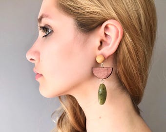 May include: A pair of dangle earrings with a wooden half-circle and a green oval-shaped stone. The wooden half-circle is brown and the stone is a mottled green color.