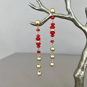 May include: A pair of long, dangling earrings with red and gold beads. The earrings are hanging from a metal stand.