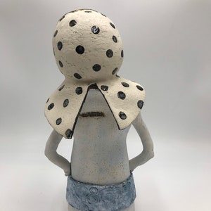 K&ouml;nnte beinhalten: Eine wei&szlig;e Keramikfigur einer Person mit einem gro&szlig;en, wei&szlig;en, gepunkteten Hut und einem blauen, gemusterten Rock.