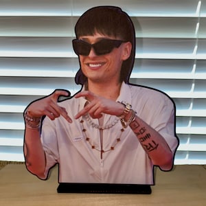 May include: A cardboard cutout of a person wearing a white shirt, black sunglasses, and a gold chain. The person has a tattoo on their arm that says "FCK DNM 121".