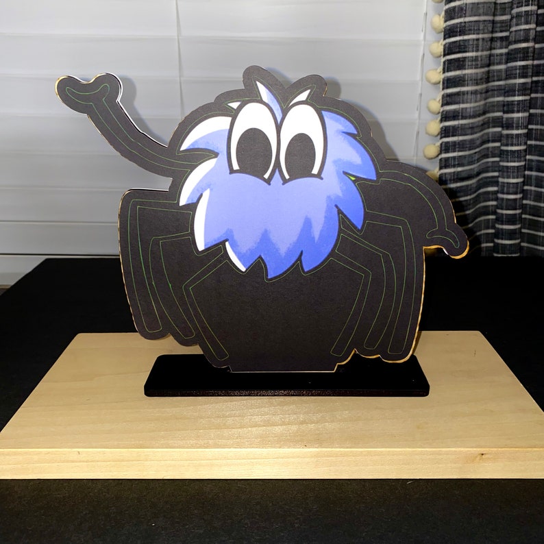 May include: A black and blue spider cutout with a fuzzy blue head and large eyes. The spider is standing on a wooden base.