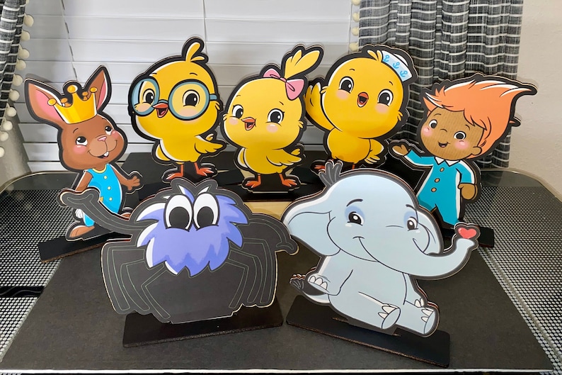 May include: A set of seven colorful cardboard character cutouts, including a spider, an elephant, a bunny rabbit, and four chicks. The cutouts are on black stands and are perfect for a children's party or classroom decoration.