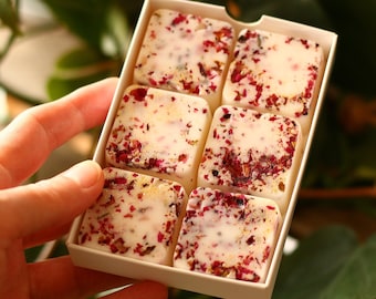 May include: A box of six white wax melts with dried rose petals and gold flecks. The wax melts are in a white box with a white lid.