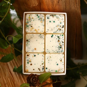 Könnte beinhalten: Ein Set mit sechs weißen Wachs-Schmelzen in einer weißen Box. Die Wachs-Schmelzen sind mit grünem und goldenem Glitzer verziert.