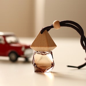 May include: A small, clear glass bottle with a geometric design, topped with a wooden pyramid and a brown cord. The bottle is filled with a light brown liquid. A small red toy car is in the background.