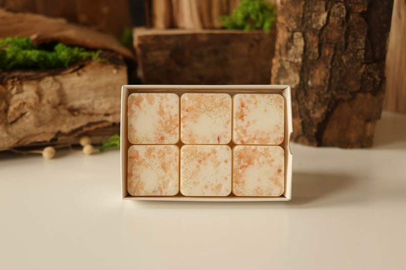 K&ouml;nnte beinhalten: Eine wei&szlig;e Box mit sechs quadratischen Wachs-Schmelzen mit einem hellbraunen und goldenen Muster.
