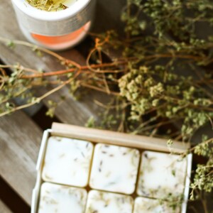 Puede incluir: Una caja de seis peque&ntilde;os jabones cuadrados blancos con hierbas y flores secas incrustadas. Los jabones est&aacute;n dispuestos en dos filas de tres. La caja es de cart&oacute;n y tiene un color marr&oacute;n natural. Los jabones est&aacute;n sobre una superficie de madera con hierbas y flores secas esparcidas alrededor.
