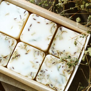 Puede incluir: Seis barras cuadradas de jab&oacute;n blanco con hierbas y flores secas incrustadas en el jab&oacute;n. Las barras de jab&oacute;n est&aacute;n dispuestas en una caja forrada con papel marr&oacute;n.