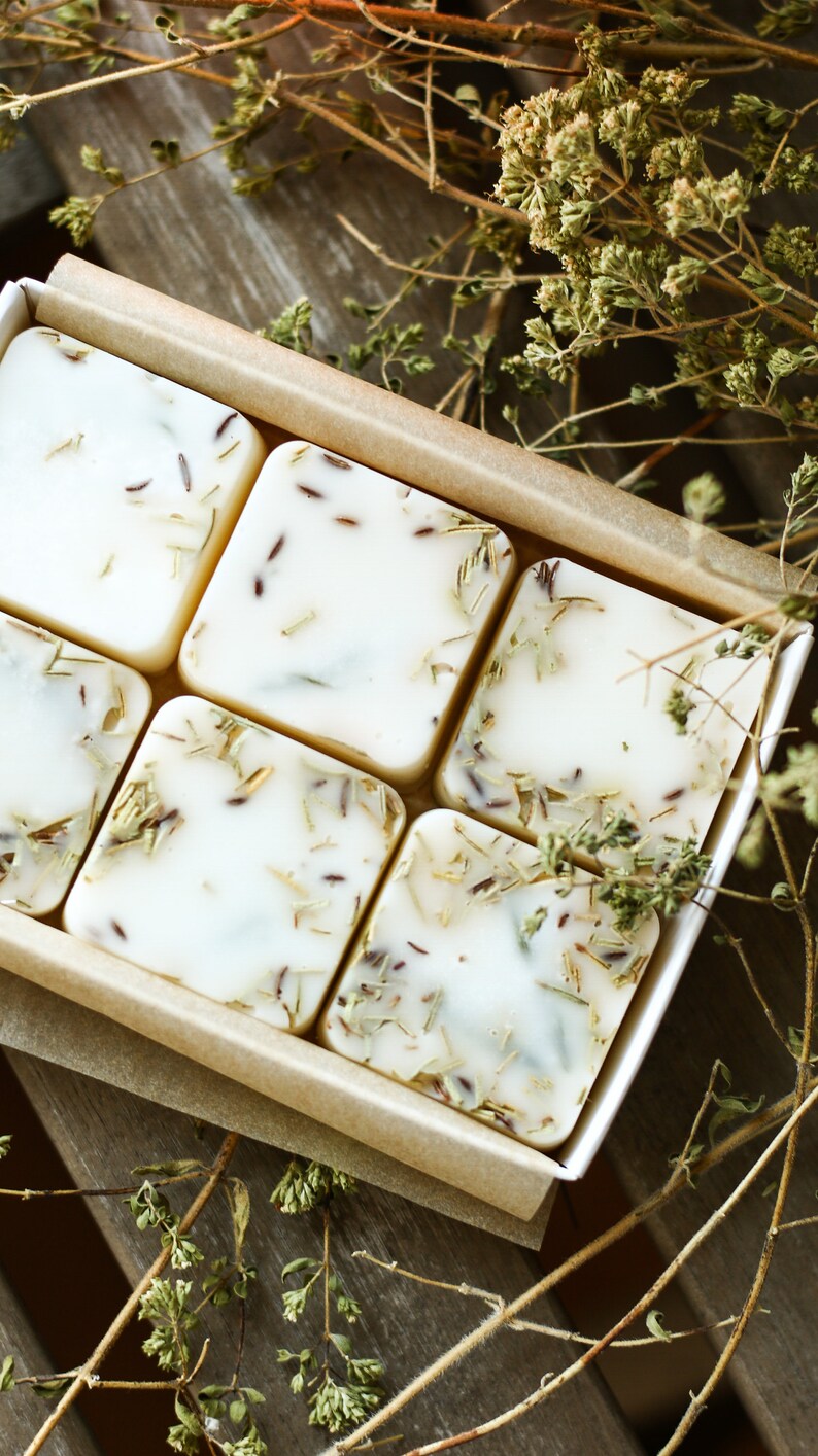 Puede incluir: Seis barras cuadradas de jab&oacute;n blanco con hierbas y flores secas incrustadas en el jab&oacute;n. Las barras de jab&oacute;n est&aacute;n dispuestas en una caja forrada con papel marr&oacute;n.