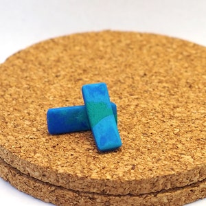 Puede incluir: Dos pendientes rectangulares de arcilla polimérica azul y verde sobre un posavasos de corcho.